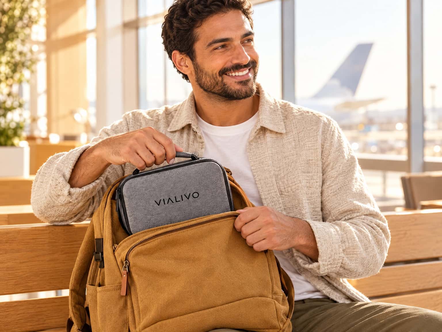 A person at an airport gate slides a grey Vialivo Crate 10 into a backpack's front pocket